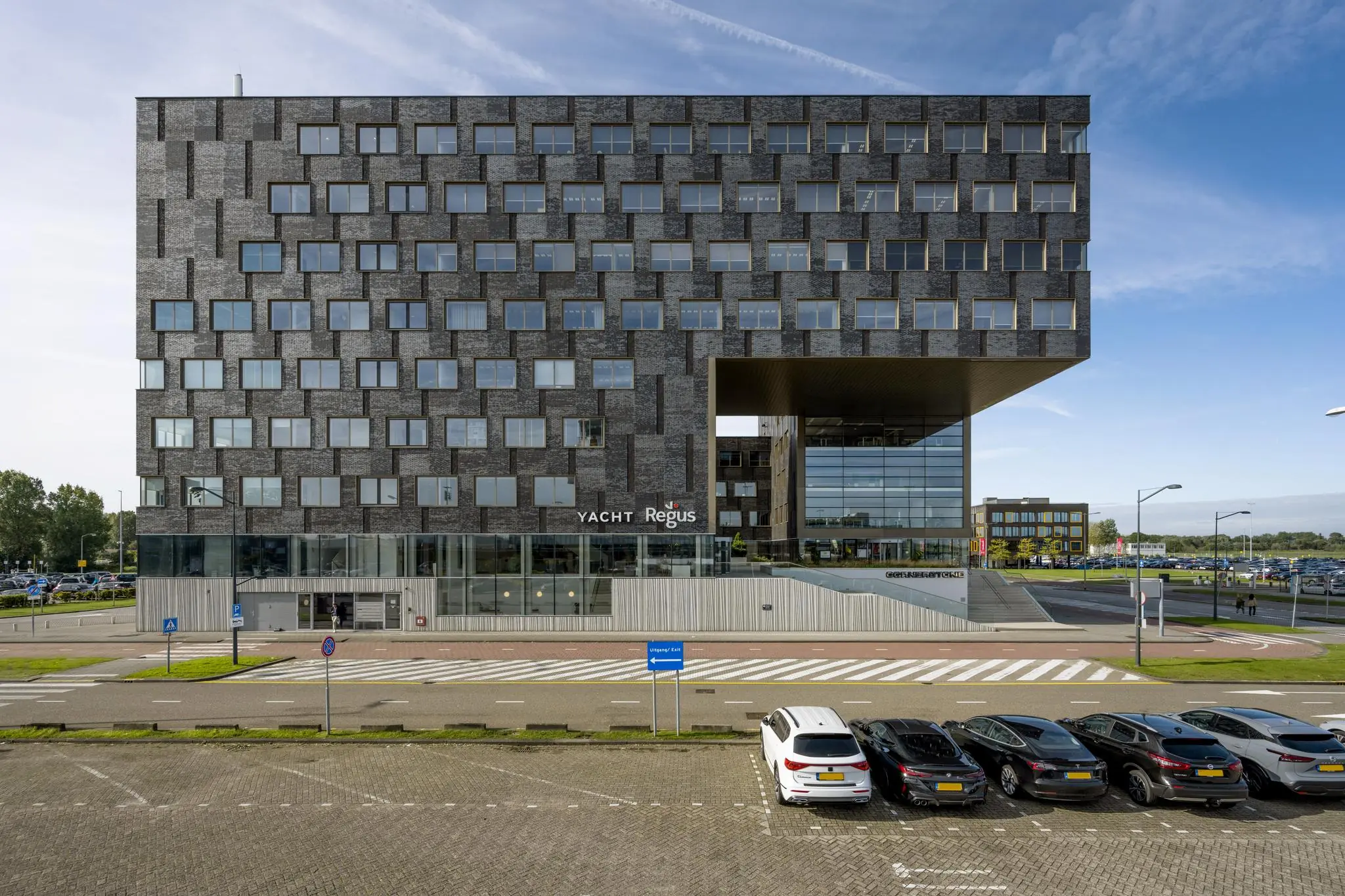 Modern kantoorgebouw aan het Rotterdam Airportplein met opvallende gevel en parkeerplaatsen op de voorgrond.